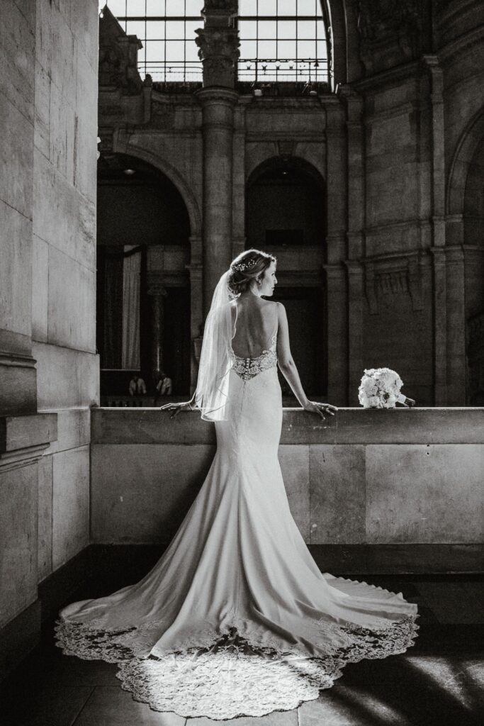 Hochzeitsfotograf Hannover: Elegante Braut von hinten im Brautkleid mit langer Schleppe vor der Architektur des Neuen Rathauses in Schwarz-Weiß